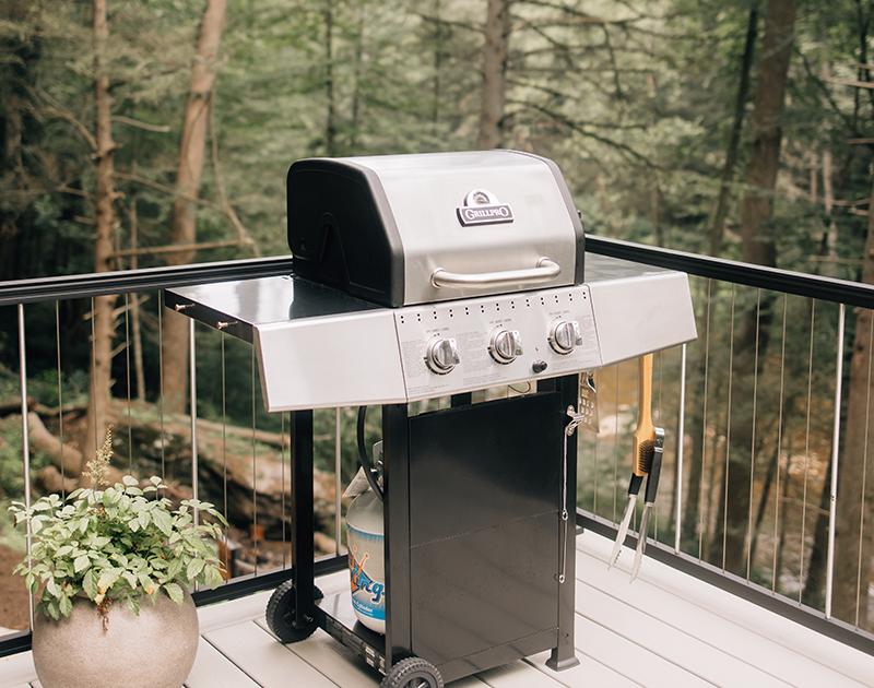 Propane grill on composite deck with aluminum vertical cable railing overlooking wooded area