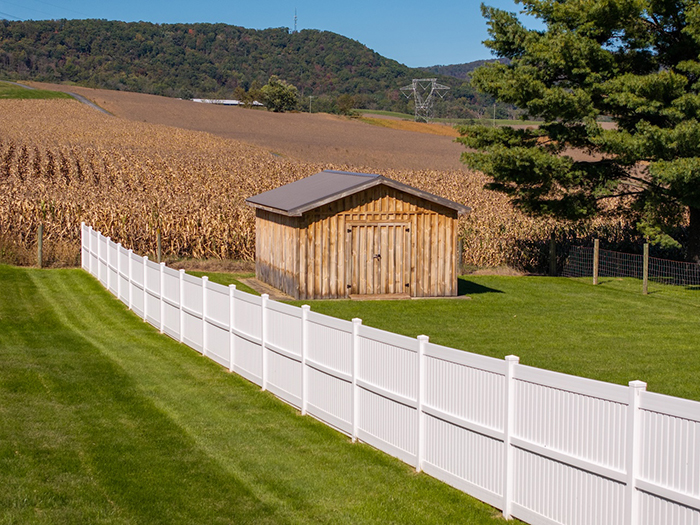 White vinyl semi privacy fence in country side with corn field and mountains in the background